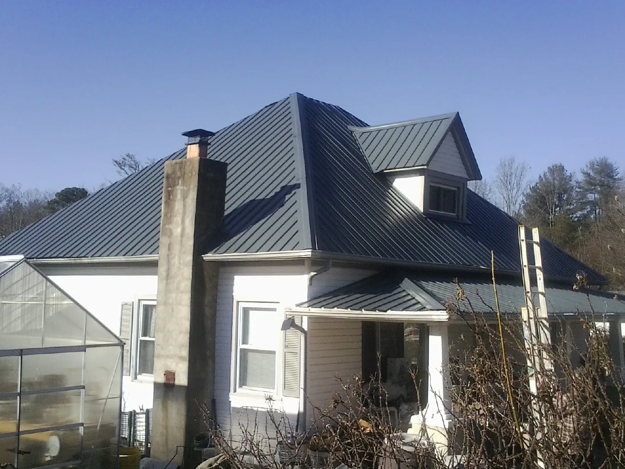Dark blue standing seam metal roof on a white farmhouse with dormer — Slate & Tile Roof Repair by Roofing Brothers in Friendswood