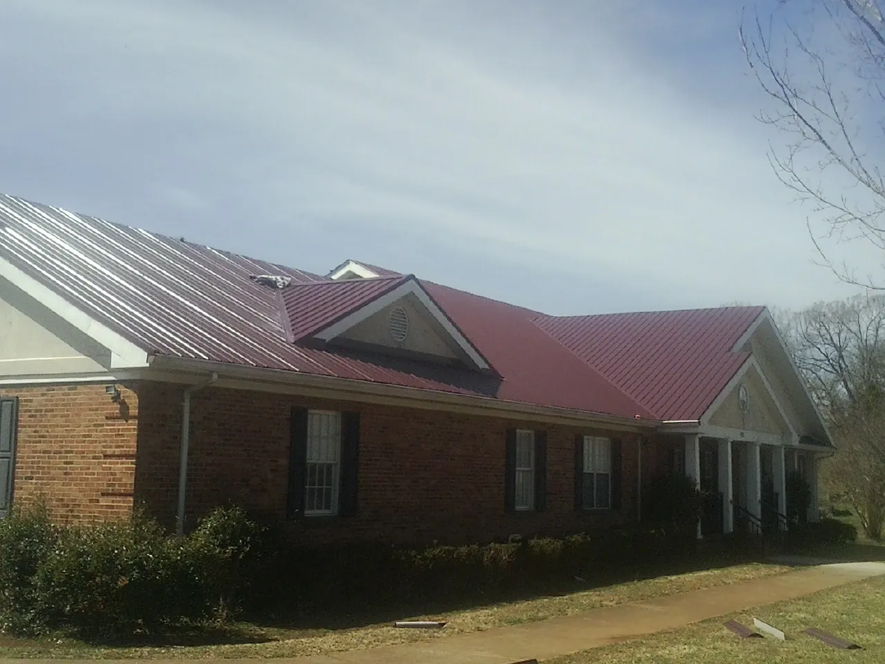 Red metal roof with gabled entries on a long brick building, from a Hail Damage Roof Repair job in Friendswood