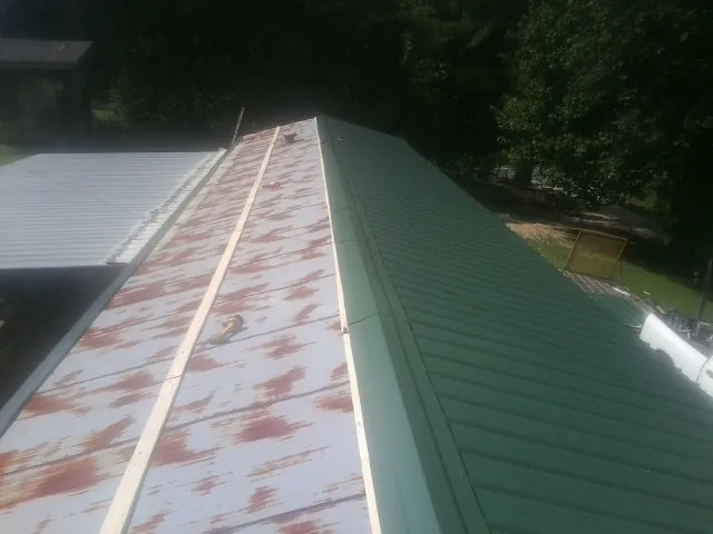 Old rusted panels beside newly installed green metal roofing — Wind Damage Roof Repair by Roofing Brothers in Friendswood