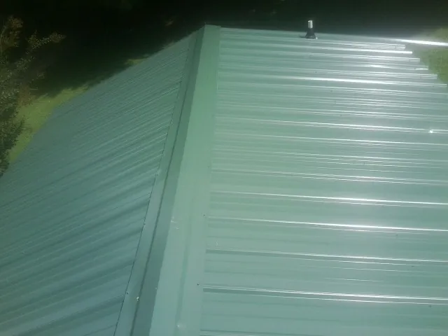 New green metal panels meeting at the ridge of a roof — Flat Roof Repair work by our crew in Friendswood