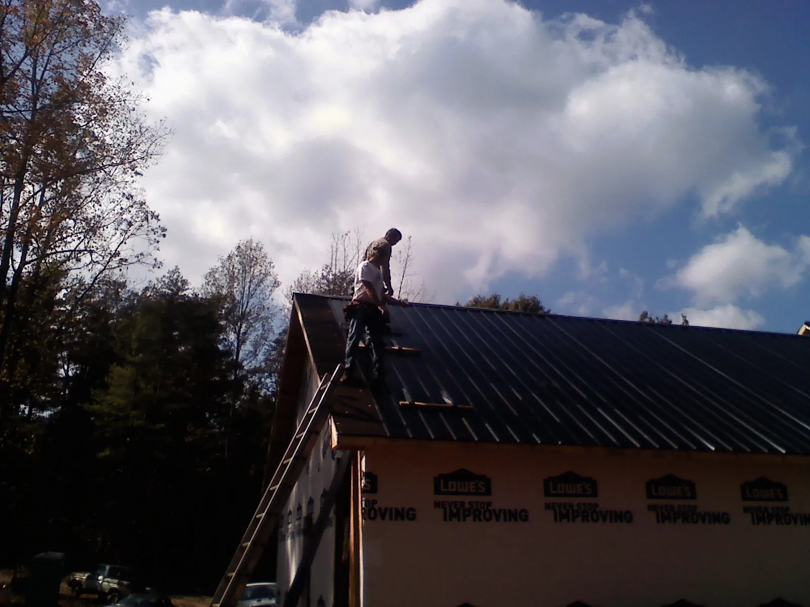 Roofer fastening dark metal panels high against a cloudy sky, from a Roof Inspection job in Friendswood