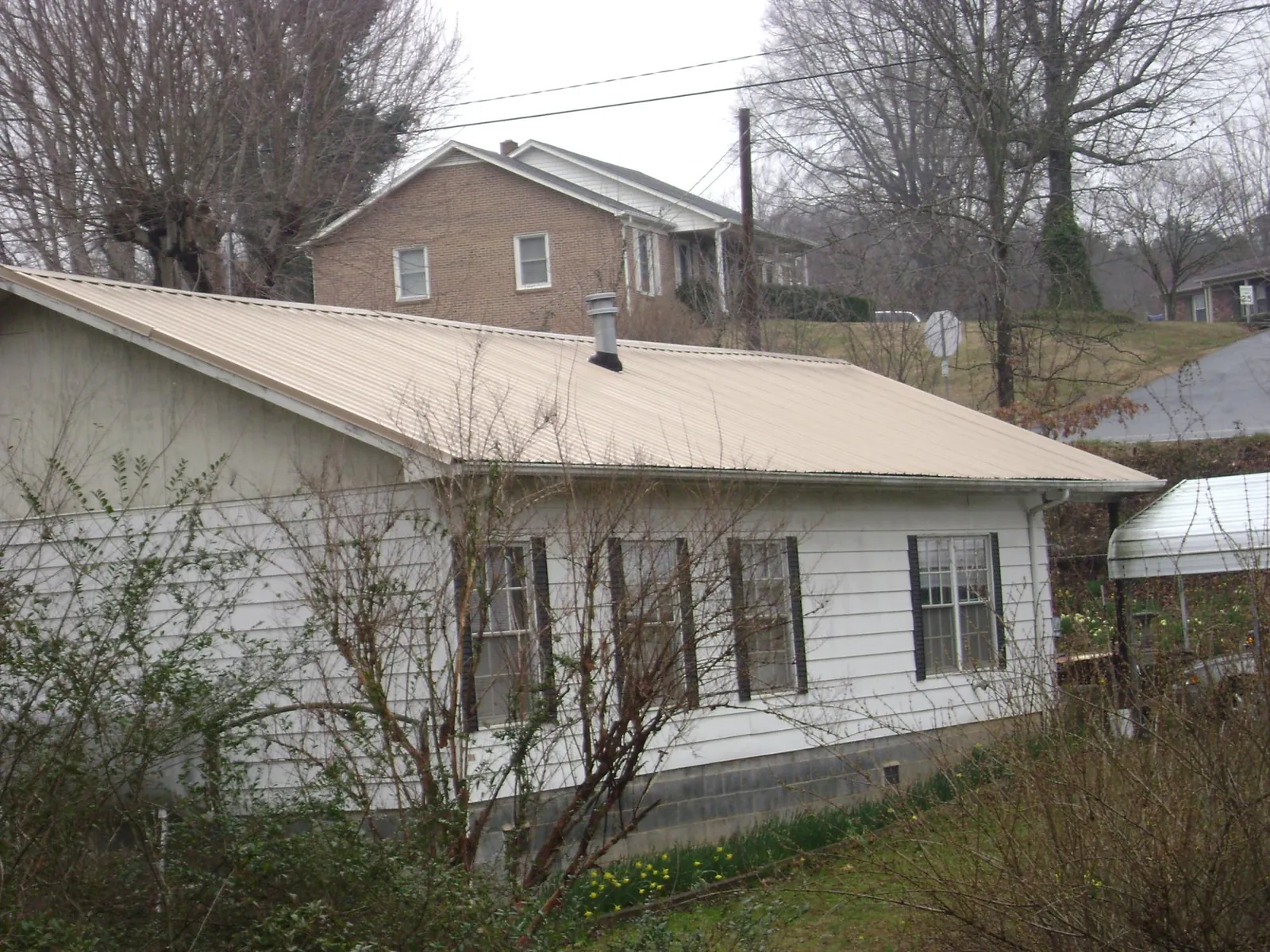 Tan metal roof on a white sided house set into a hillside — Commercial Roofing by Roofing Brothers in Friendswood