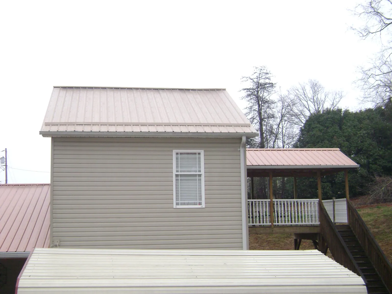 Tan metal roofs on a two story addition and attached porch, from a Roof Replacement job in Friendswood